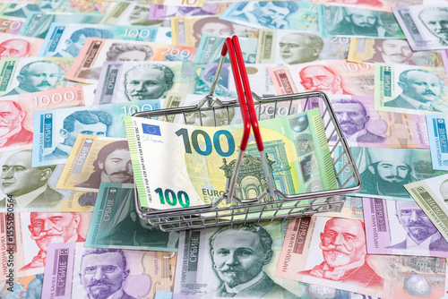 Shopping basket with a 100 euro bill on a pile of Serbian paper money