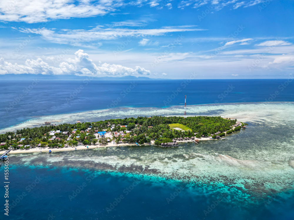 Fototapeta premium Picturesque Tropical Island with Village and Jetty Surrounded by Clear Blue Waters and Coral Reefs in Indonesia