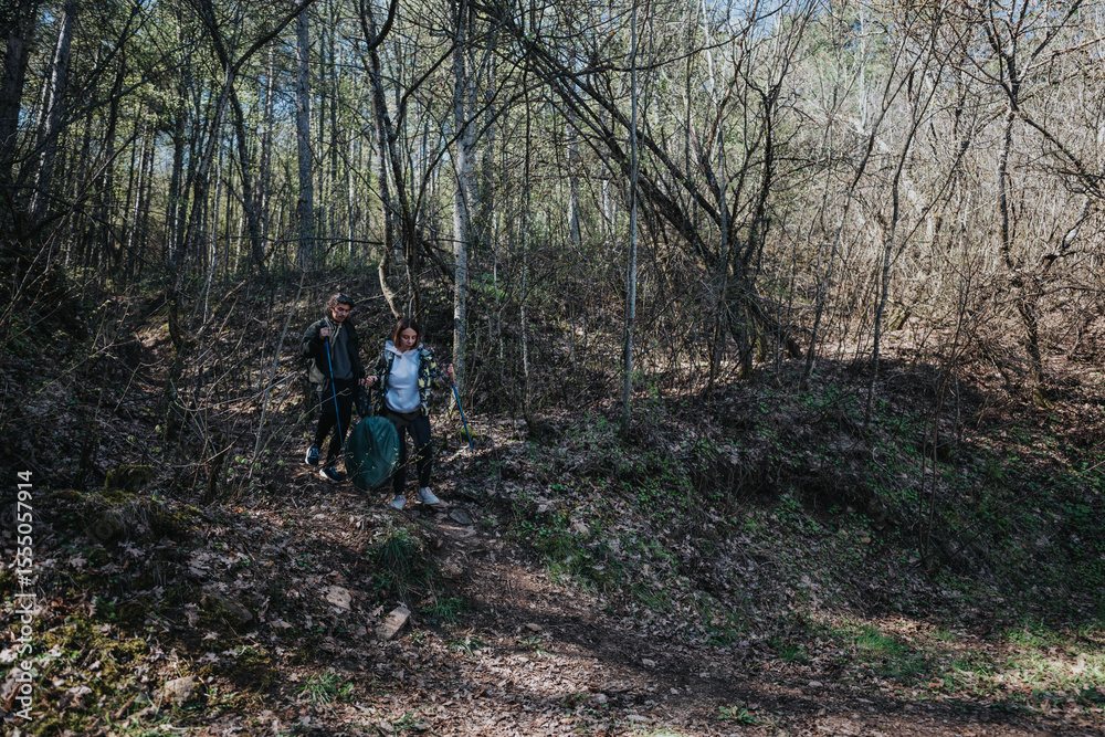 Obraz premium A man and woman venture through a wooded area, equipped with backpacks and walking poles, on a serene hiking excursion to connect with nature.