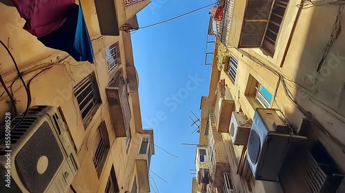 Vertical housing blocks with laundry lines and air conditioners, tight alley upward view with faint blue sky  photo