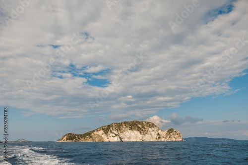 An enchanting island emerges from calm waters, framed by an expansive sky filled with fluffy clouds, creating a peaceful coastal retreat that invites exploration