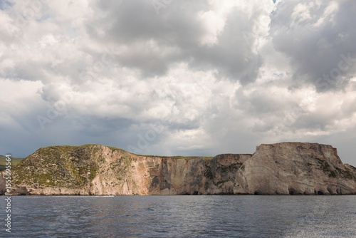 Towering cliffs stretch along the serene coastline, kissed by gentle waves. Dark clouds loom overhead, adding intensity to the coastal landscape as nature unfolds its beauty