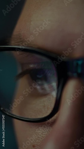 Close-up view of concentrated eyes behind glasses, fixated on a brightly lit computer screen at night. The individual is immersed in digital work or exploration, highlighting dedication