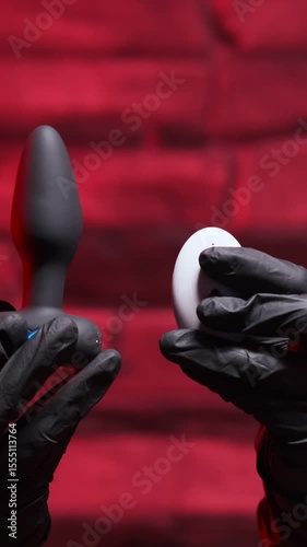 Silicone anal plug with a remote control rotates in a female hand in black latex gloves on a black background. Massager with multiple speeds. Sex shop products, adult gifts for couples
