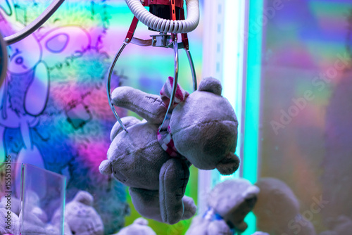 A soft teddy bear is currently hanging from a claw machines grip