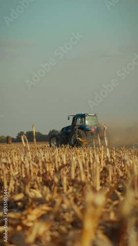 A tractor works diligently in a dusty field during harvest time, gathering crops as the sun sets over rural farmland, showcasing a busy agricultural scene and the beauty of nature