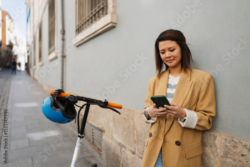 Asian woman using e scooter and app while exploring new city