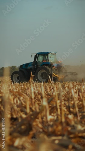 A tractor works through a cornfield at sunset, tilling the soil in preparation for planting. Dust rises as the vehicle moves across the golden landscape, enhancing the serene atmosphere of rural life