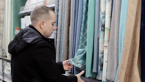 Customer exploring fabric textures, comparing curtain colors, touching materials with fingertips while browsing textile store showroom with bright illumination