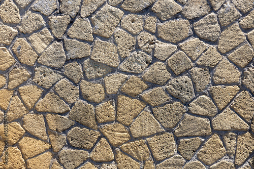 Cracked stone structure. Textured background illuminated by the sun. Irregular stones