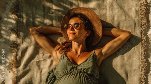 Relaxed woman enjoying sunlight on a beach, wearing sunglasses and a straw hat.