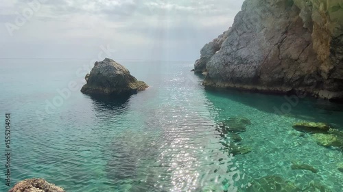 Small sea ripples shimmer under the bright sun near coastal rocks. A peaceful marine scene highlighting nature's sparkle, ideal for travel, relaxation, and coastal lifestyle themes.