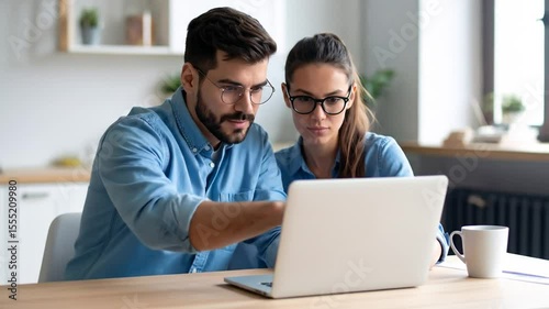 Engaged young couple collaborating using a laptop in their modern kitchen at home