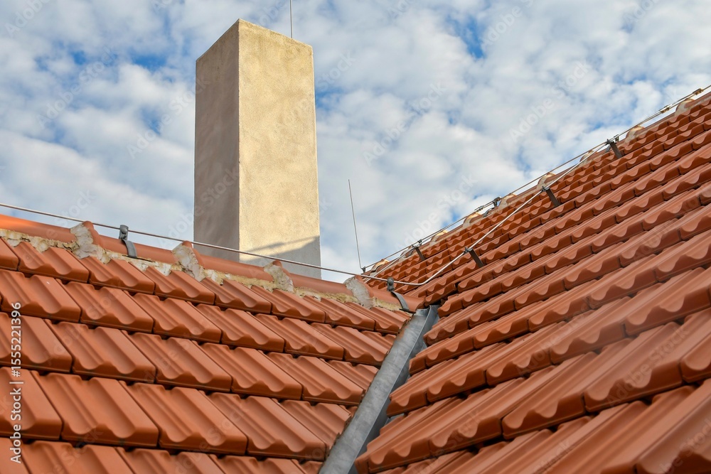 Naklejka premium Newly covered roof. New roof covering with burnt red tiles and a chimney on the roof. Industrially manufactured tiles on the new roof. Concept of construction, building work, and renovation of the ho