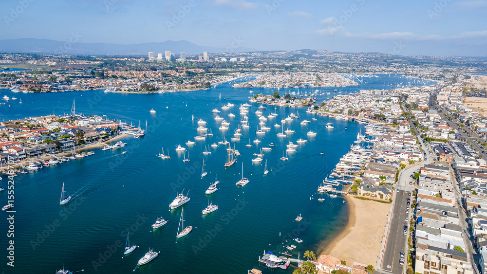 Fototapeta premium Scenic Aerial View of Newport Bay in Orange County, California – Coastal Harbor with Yachts, Waterfront Homes, and Blue Ocean Waters Under Clear Skies – Drone Photography of Newport Beach