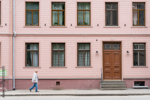 elderly man walking past pink residential building with large wooden door and symmetrical windows in urban city street minimal architecture concept daytime lifestyle exterior old town europe scene