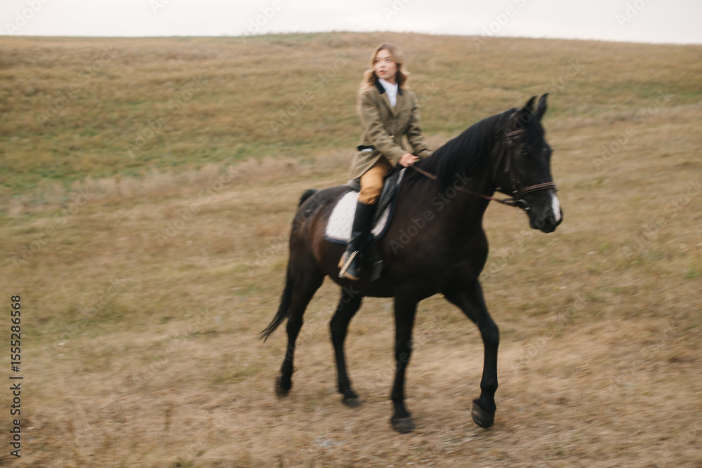Obraz premium Woman Riding Black Horse Across Open Grassland Fields Near Hillside