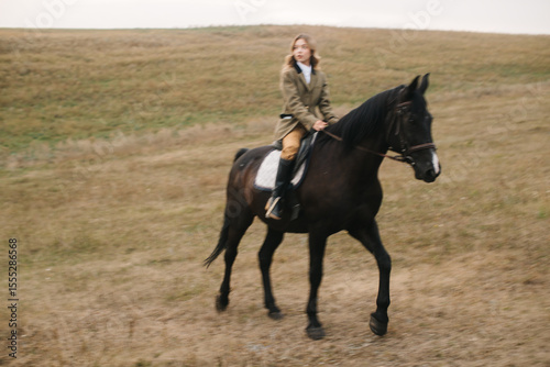 Woman Riding Black Horse Across Open Grassland Fields Near Hillside
