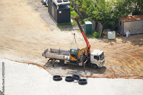 Aerial view of a construction site with a mobile crane truck lifting a mini excavator. Industrial construction machinery in action, transportation of heavy equipment