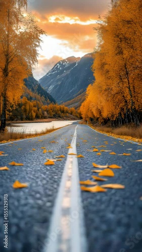 Autumn Road With Fallen Leaves Surrounded By Vibrant Orange Trees Leading Toward Snowy Mountain Peaks Under Colorful Sky

