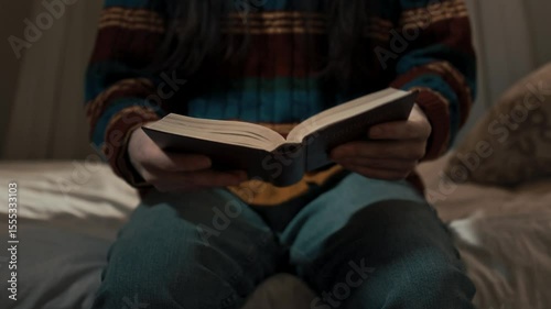 Man in a brightly knitted sweater holds the holy book of the Bible in his hands and reads it