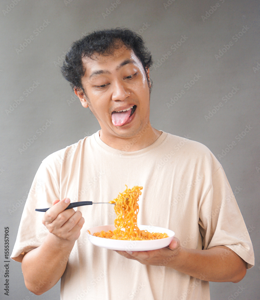 Portrait of handsome asian man eat instant noodle on grey background. He's feel surprise and excited with how delicious it is Portrait of handsome asian man eat instant noodle on grey background. He's feel surprise and excited with how delicious it is