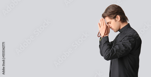 Young priest praying with beads on dark background