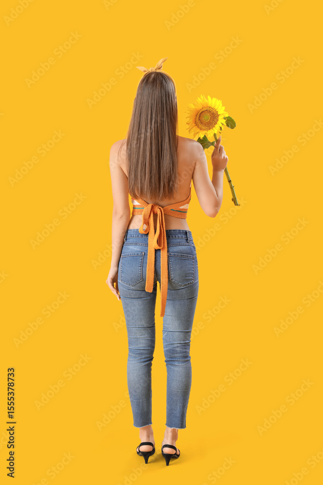Fototapeta premium Young woman with beautiful sunflower on yellow background, back view