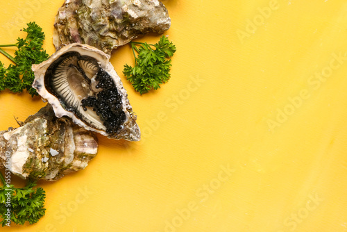 Tasty oysters with black caviar on yellow background