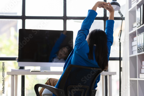 Businesswoman working on computer at office. She was stretching to relieve herself from sitting in an office chair for a long time.
