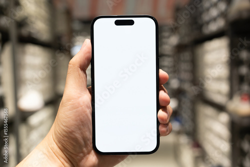Hand Holding Blank Smartphone Screen in Retail Store. Mobile shopping, online commerce, in-store digital experiences, product information lookup, or advertising with a customizable screen.