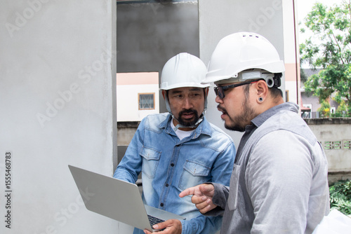 Hispanic engineer man with mustache wearing safety white helmet consult team project manager partnership, Asian foreman standing in construction site building reading blueprint and laptop technology