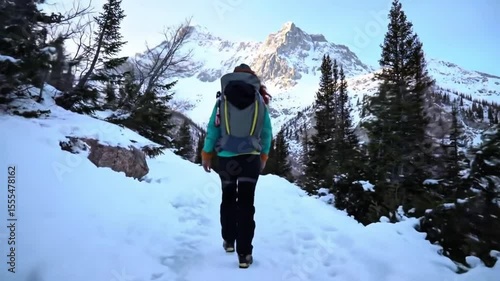 Solo hiker walking on snowy mountain trail in winter forest