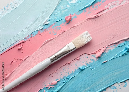 A clean white paint brush rests on thick, creamy pastel pink and blue paint strokes.