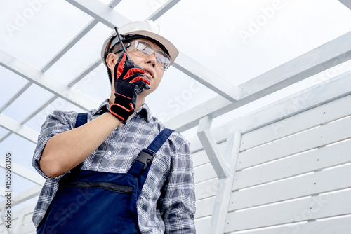 Confident Asian man civil engineer looking forward and talking on walkie talkie. Smart male foreman using radio communication equipment at construction site for cooperation with the worker team