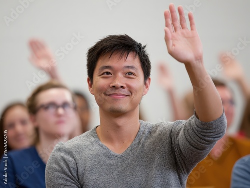 Smiling Asian man in 20s raising hand in a meeting with diverse people