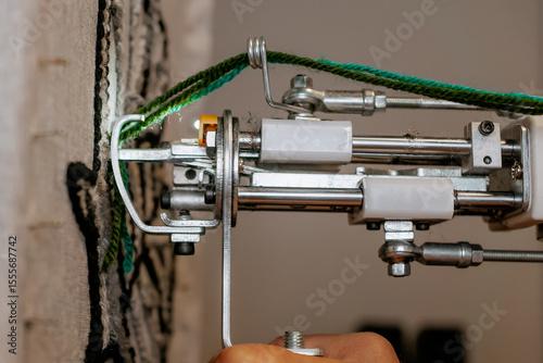 Close-up of a hand-held tufting gun being used to create a rug with green yarn, showing detail of industrial textile equipment and DIY carpet making process