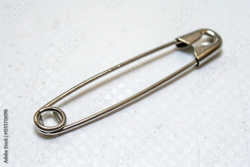 Clean metallic safety pin, a fundamental fastener, placed on white stationery, for everyday utility