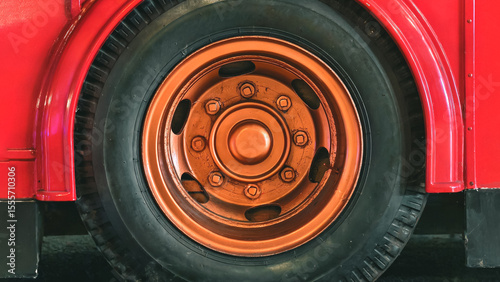 Striking detail of a vintage red vehicle featuring a prominent orange wheel, conveying nostalgia