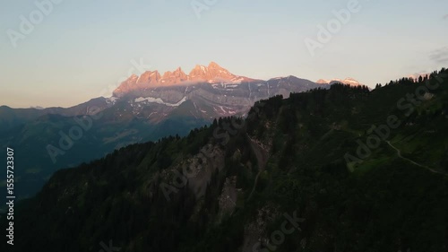 Beautiful Sunset drone flight in the Swiss Alps. Drone pans behind the tree line looking at the pink sunset on the peaks of the Dents du Midi in the Val d'Illiez of Canton Valais in Switzerland.