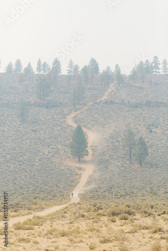 Mountain biker riding down hill on dirt road in smoky landscape