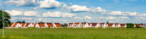 Panoramafoto einer Neubausiedlung mit Doppelhaushälften am Feldrand bei schönem Wetter und aufgelockerter Bewölkung