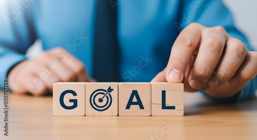 Man in blue shirt arranging wooden blocks spelling GOAL with a target icon, focusing on setting and achieving personal or business objectives.