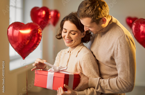 Valentine day gift box giving, love feeling, romantic surprise, happy loving couple in tender hug, kiss, man, woman, heart shaped red balloon foil decor, wedding party room decoration, making proposal