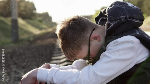 Sad boy sits on the railway in a bad mood after school. Childhood depression, headache and migraine, bullying.