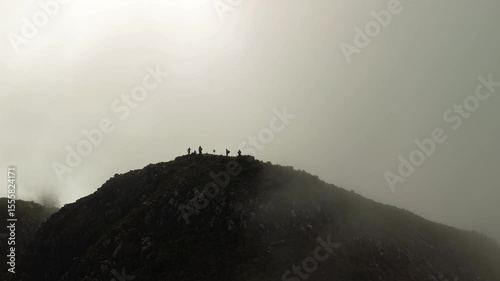 Silhouetted trekkers stand on Mount Apo’s rocky first peak as dawn light pierces drifting fog and clouds, framing a dramatic high-altitude ridge above the valleys of Mindanao.