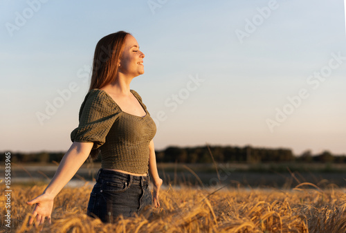 Young redhead woman breathing fresh air in a wheat field at sunset