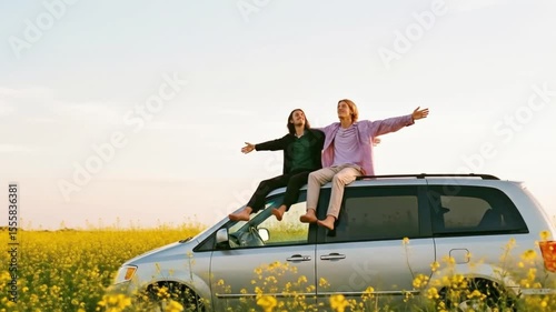 Two carefree young men sit on top of a minivan in a field of yellow flowers