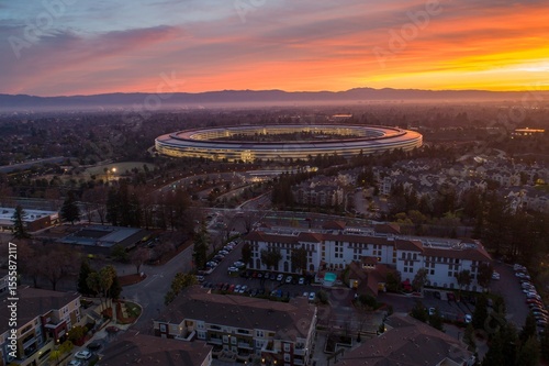 Aerial view of Apple Park at sunrise in Cupertino, California, USA. The corporate headquarters is lit up as employees arrive for work.