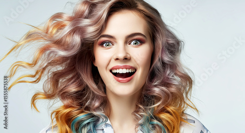 Young woman with vibrant, wavy hair is smiling joyfully, showcasing her colorful hairstyle against a soft, neutral background, embodying happiness and self-expression